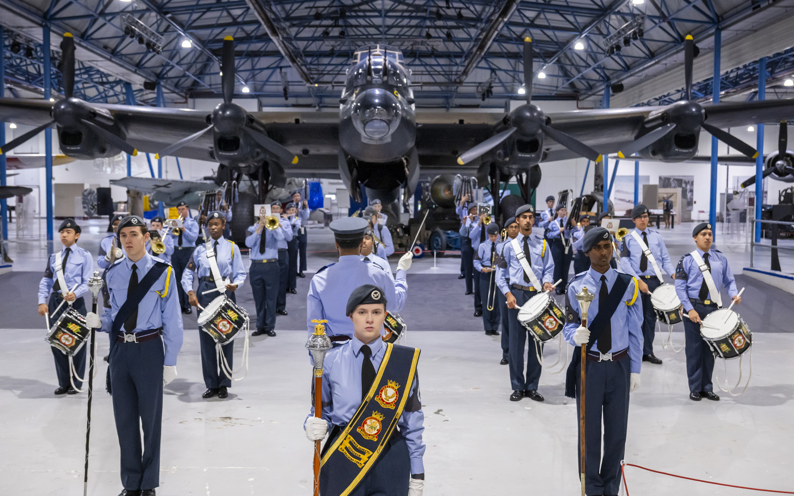 A military band performing inside an aircraft hanger, large plane in background.