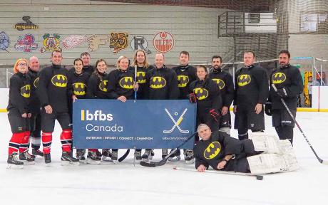 Hockey players posing on the ice wearing batman t-shirts.