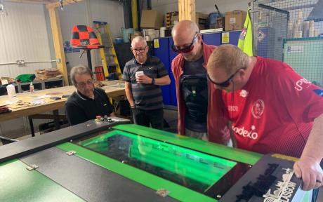 Group of veterans using a laser machine in a workshop.