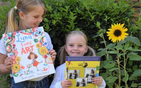 Two young girls smiling and holding up books.
