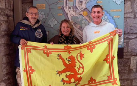 Photo of three people holding up a yellow flag with a red dragon on it.