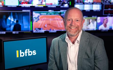 PR photo of BFBS CEO Ben Chapman, multiple TV screens in background.